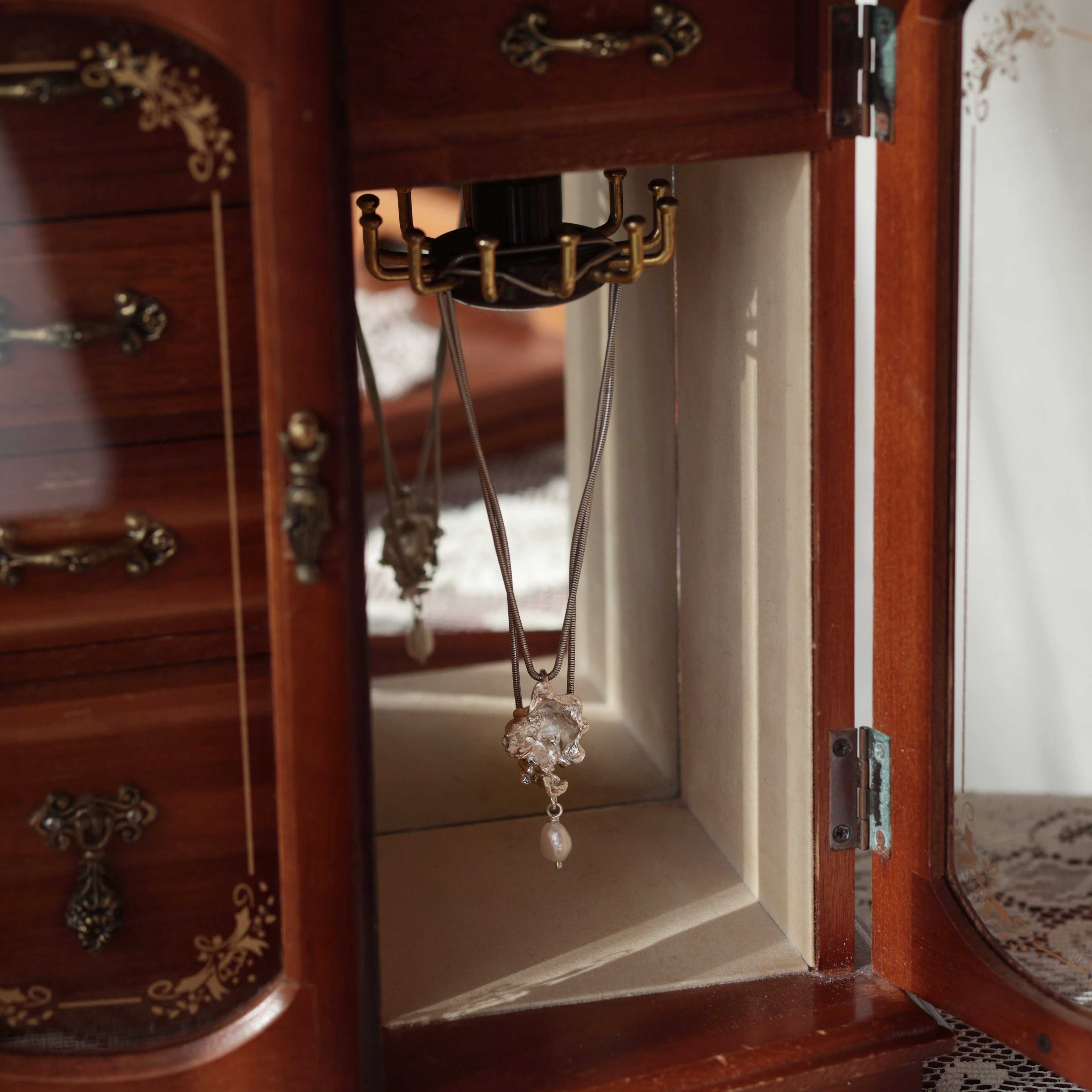 Organic silver and pearl necklace hanging in wooden jewellery box