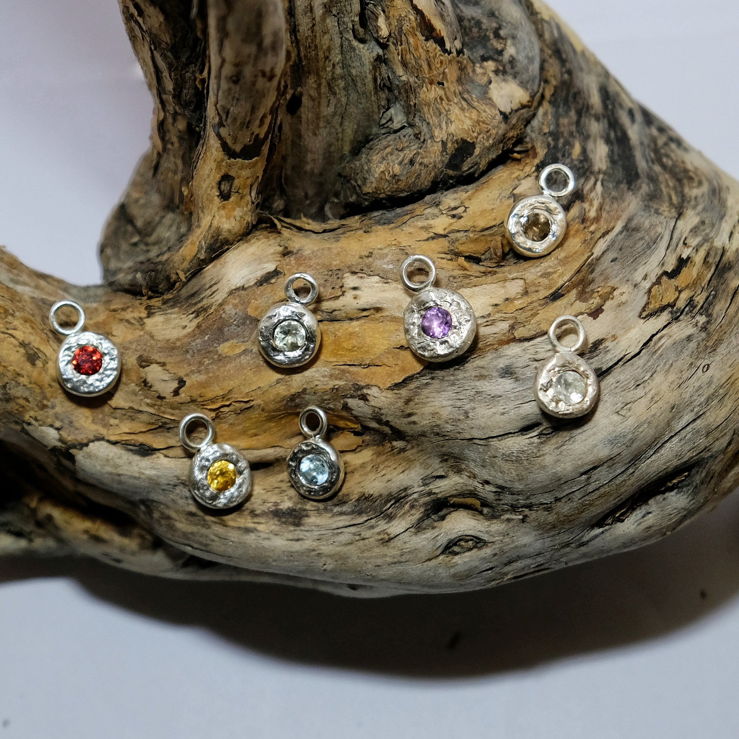 Handmade silver charms with colourful gemstones laying on driftwood | Made with Grace | handmade jewellery nz